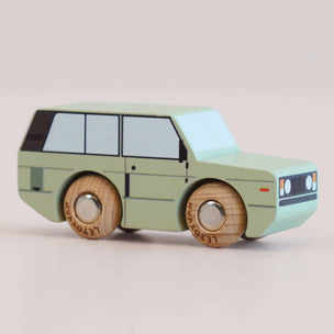 Wooden toy car with a light green body and brown wheels on a beige background
