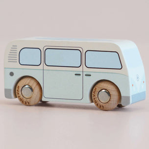 A wooden toy bus with a pastel cream and light blue color scheme, featuring natural wood wheels with engraved lettering, shown on a neutral beige background.