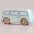 A wooden toy bus with a pastel cream and light blue color scheme, featuring natural wood wheels with engraved lettering, shown on a neutral beige background.