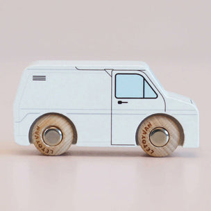 A wooden toy van with a white body and natural wood wheels, shown from the side against a soft beige background.