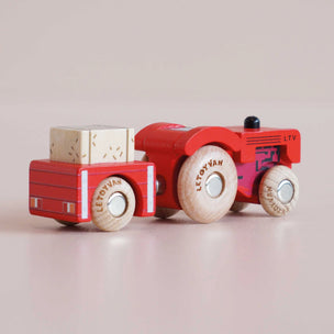 Wooden toy truck with red body and beige wheels on a light pink background