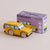 A yellow miniature toy van with realistic wood-textured wheels, positioned in front of its purple packaging box labeled 'GT195 RILEY' on a solid beige background.