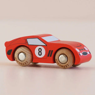 Red toy race car with wooden wheels on a beige background