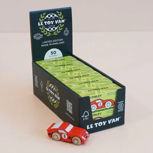 A display box of Le Toy Van limited edition wooden toy cars, with a red and white race car placed in front on a light beige background.