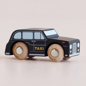 a black taxi toy car sideways with. a beige background 