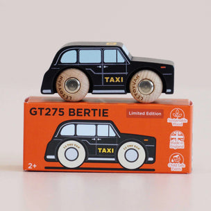 A black wooden toy taxi car with light wood wheels sits on top of its orange retail box. The box shows the text 'GT275 BERTIE' and 'Limited Edition' along with product feature icons.