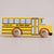 A yellow wooden toy school bus with black lettering that reads 'SCHOOL BUS LE TOY VAN' and natural wood wheels, shown on a plain light beige background.