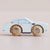 A wooden toy car with a pale blue body and natural wood wheels, shown in profile against a soft beige background. The wheels are branded with the text 'LETOISIAN'.