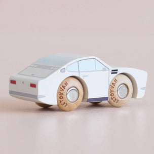 A small wooden toy car with a white body, light blue roof and windows, gray bumper and stripe details, and natural wood wheels printed with the word 'MAYBAUM'.