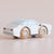 A small wooden toy car with a white body, light blue roof and windows, gray bumper and stripe details, and natural wood wheels printed with the word 'MAYBAUM'.