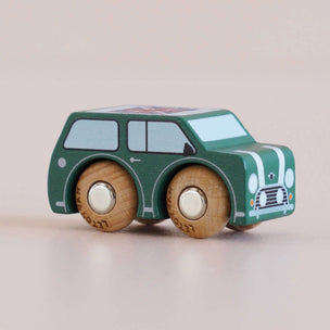 A wooden toy car styled like a classic Mini Cooper, painted in dark green with white stripes, light blue windows, and natural wood wheels, set against a soft beige background.