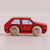 A small wooden toy car in red with natural wood wheels and black window details, photographed on a plain light beige background.