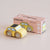 Yellow toy car next to its packaging box on a beige background