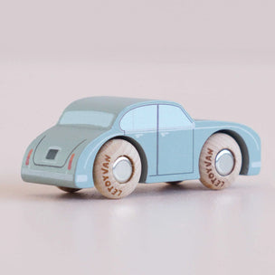 A small wooden toy car in a light blue color with natural wood wheels, shown on a soft, light pink background.