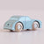 A small wooden toy car in a light blue color with natural wood wheels, shown on a soft, light pink background.
