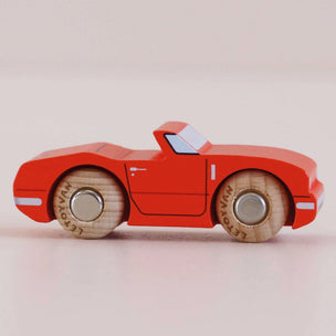 Red toy car with wooden wheels on a light pink background