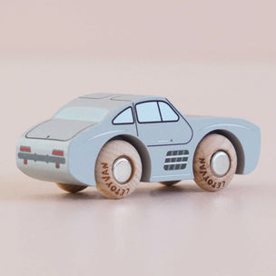 A small toy car with a light blue body and natural wood wheels, photographed on a soft beige background.