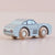 A small toy car with a light blue body and natural wood wheels, photographed on a soft beige background.