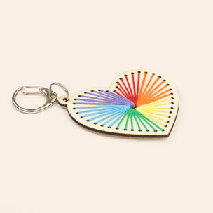 Heart-shaped keychain with rainbow string design on a beige background