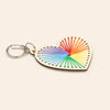 Heart-shaped keychain with rainbow string design on a beige background