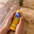 Hand holding a yellow candle object with floral design on a wooden surface with flowers in the background