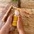 Hand holding a yellow cylindrical container with floral design on a wooden surface with flowers in the background