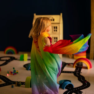 Child in a rainbow-colored cape playing with toys on a dark floor.