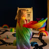 Child in a rainbow-colored cape playing with toys on a dark floor.