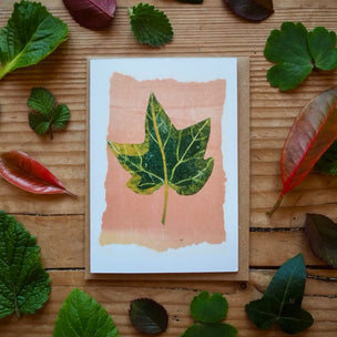 Card with leaf illustration surrounded by real leaves on a wooden surface