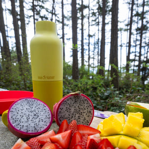 Fruit platter with dragon fruit, strawberries, and mangoes on a wooden board with a yellow water bottle in the background.