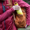 Person holding a yellow water bottle with a brown backpack outdoors