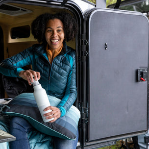 Woman sitting inside a vehicle with an open door, holding a water bottle.