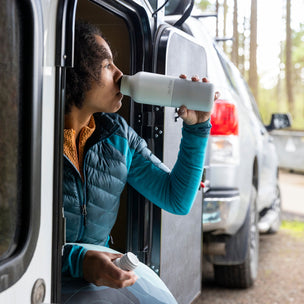 Person sitting in a vehicle, leaning out of the window, holding a bottle.