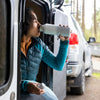 Person sitting in a vehicle, leaning out of the window, holding a bottle.