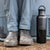 Person wearing gray pants and boots with a black water bottle next to a vehicle.