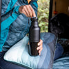 Person sitting inside a vehicle, holding a black water bottle.