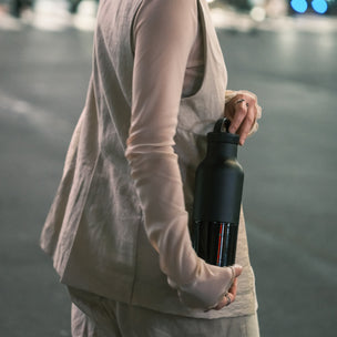 Person holding a black water bottle on a blurred street background