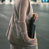 Person holding a black water bottle on a blurred street background