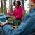 Two people sitting at a picnic table in a forest, holding colorful water bottles.