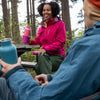 Two people sitting at a picnic table in a forest, holding colorful water bottles.