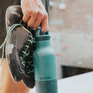 Person holding a teal water bottle with a climbing shoe on a blurred background