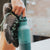 Person holding a teal water bottle with a climbing shoe on a blurred background