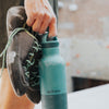 Person holding a teal water bottle with a climbing shoe on a blurred background