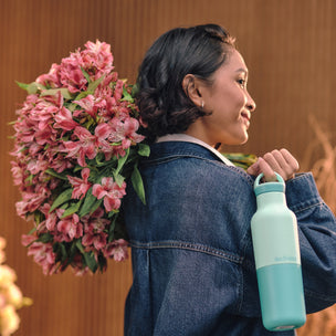 Woman holding a bouquet of pink flowers and a turquoise water bottle against a blurred background