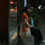 Person sitting on a bench at night holding a water bottle with a city street in the background.