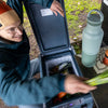 Person opening a cooler with food items including eggs and vegetables, with a water bottle nearby.