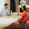 Two people sitting at a long wooden table in a modern kitchen.