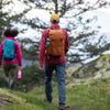 Two people hiking on a trail with backpacks in a natural setting.