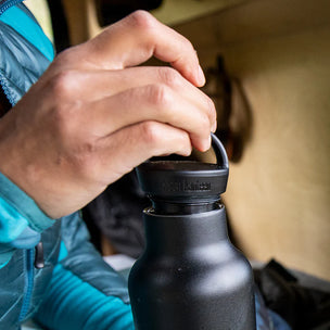 Person opening a black water bottle with a cap, wearing a blue jacket.