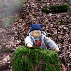Toy figure in winter clothing sitting on a mossy rock in a forest setting